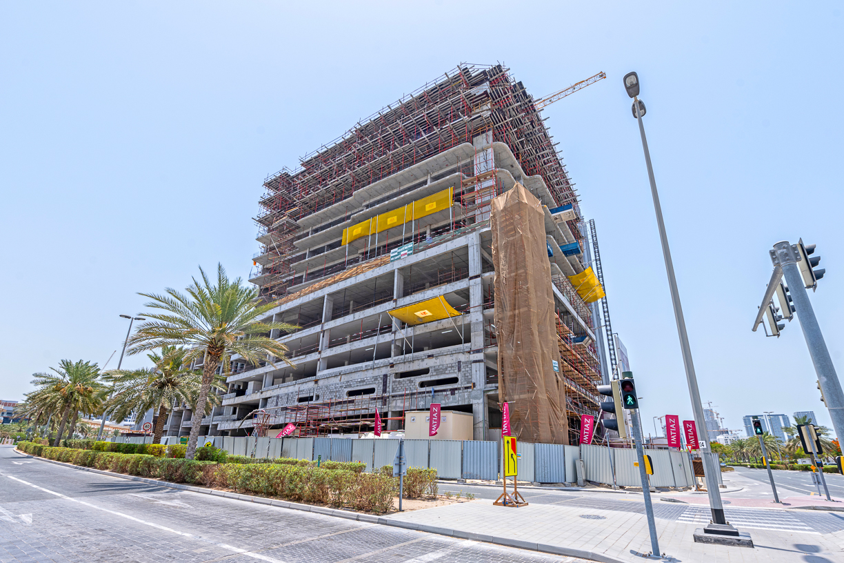 Pearl House By Imtiaz A large building under construction, featuring scaffolding, palm trees, and road signs in a sunny environment.